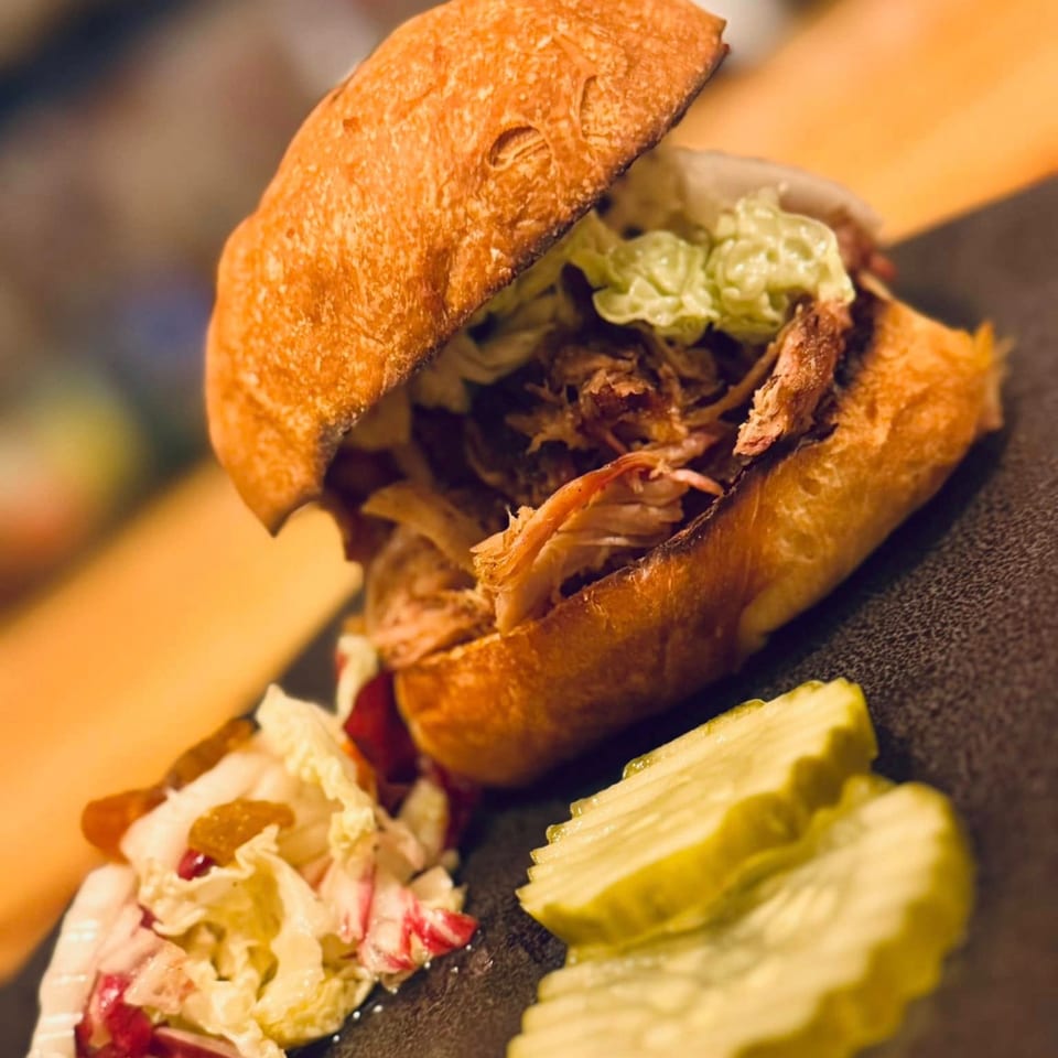 Pulled pork sandwich with coleslaw and pickles on a dark plate at United Smokehouse.