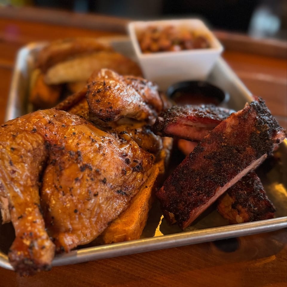A United Smokehouse platter with smoked chicken, ribs, potato wedges, and baked beans.