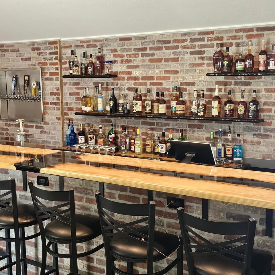 A well-stocked bar at United Smokehouse with a brick wall, wooden counter, and bar stools.
