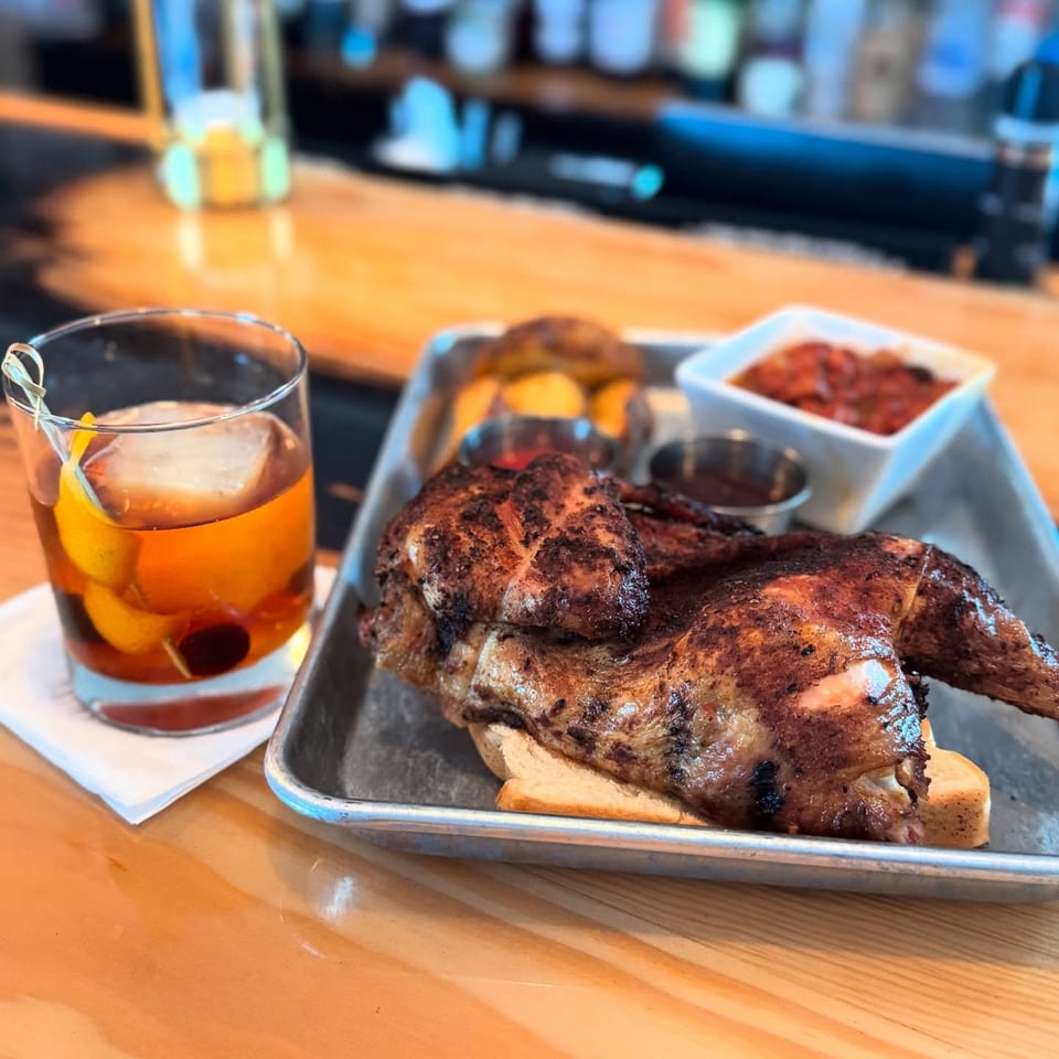 A United Smokehouse BBQ chicken platter with sides and an Old Fashioned cocktail on a bar.