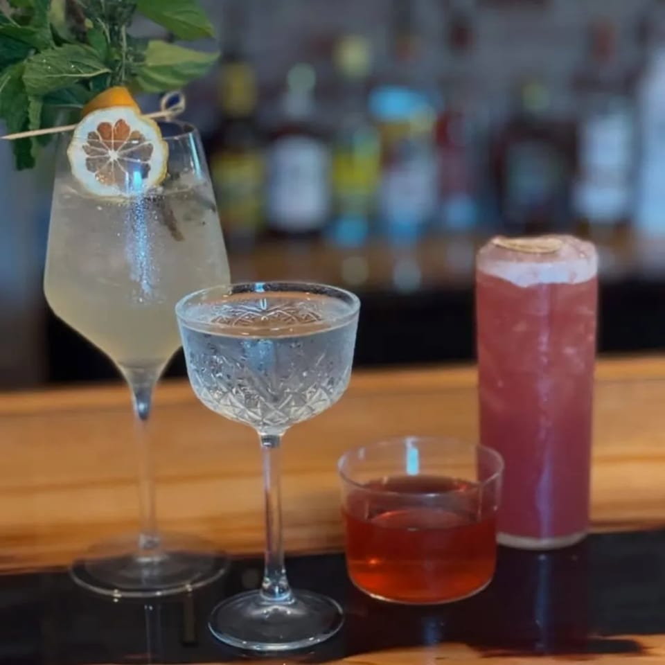 Four cocktails, including a tall garnished drink, on a wooden bar at United Smokehouse.