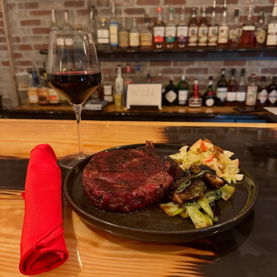 A United Smokehouse steak dinner with red wine, bok choy, and apple slaw on a bar.