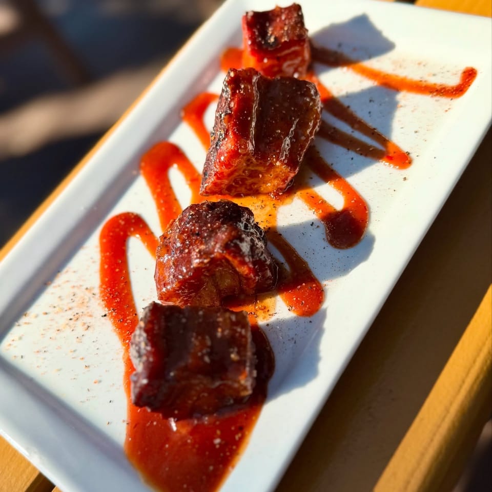 Four glistening United Smokehouse BBQ burnt ends with red sauce and pepper on a white plate.